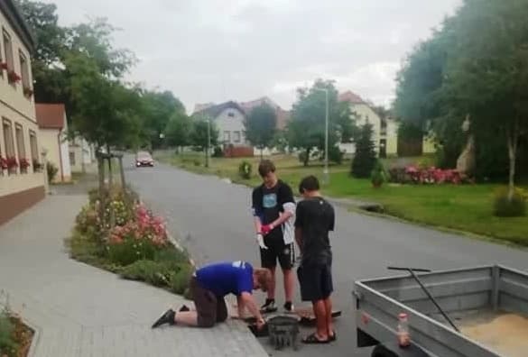 Tři muži pracují na chodníku u silnice, jeden klečí
