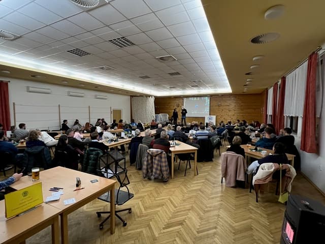 Sál plný lidí sledujících prezentaci na plátně