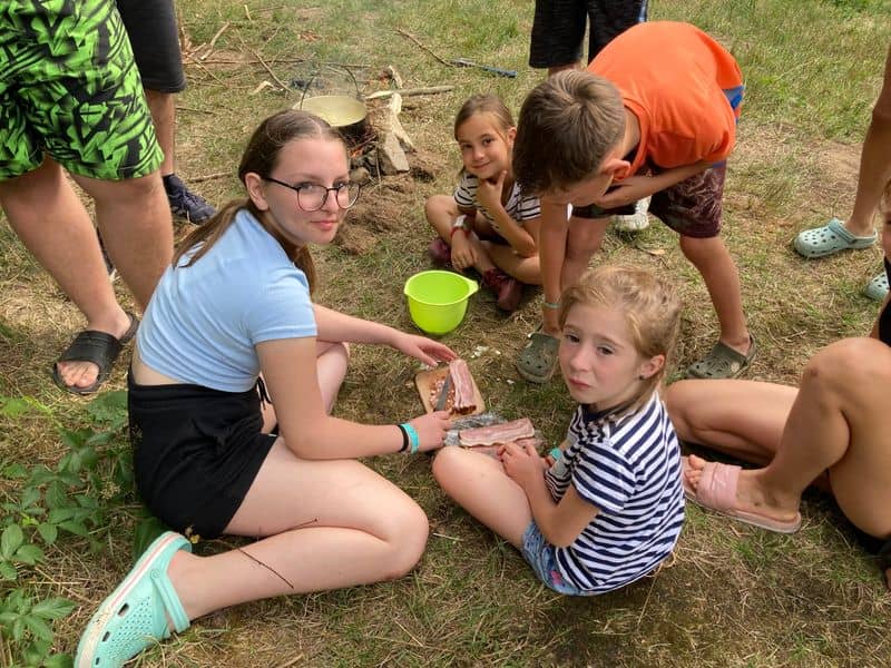 Skupina dětí připravuje jídlo u ohně